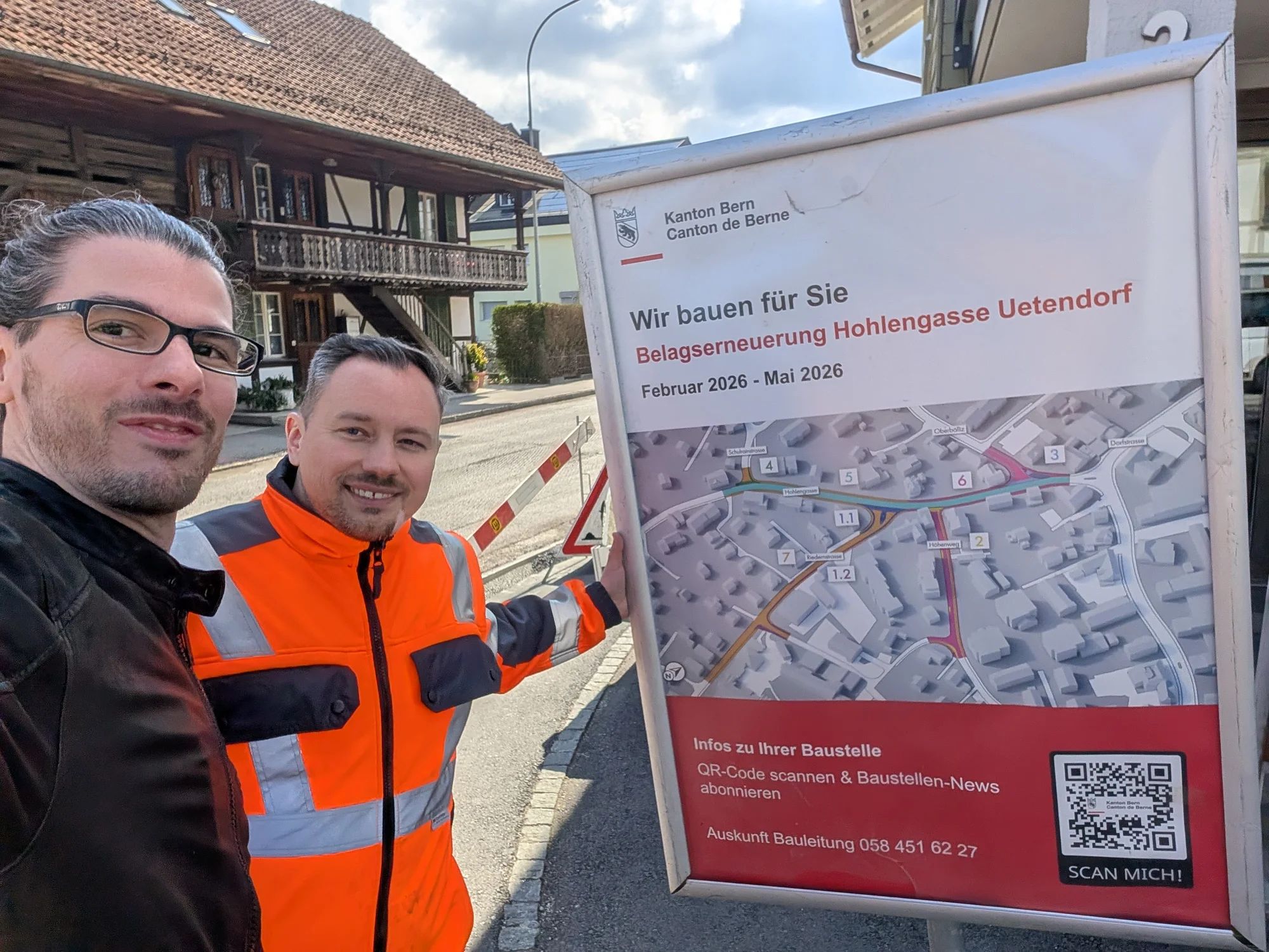 Two project team members next to the site board for the Hohlengasse resurfacing in Uetendorf, with site map and QR code.