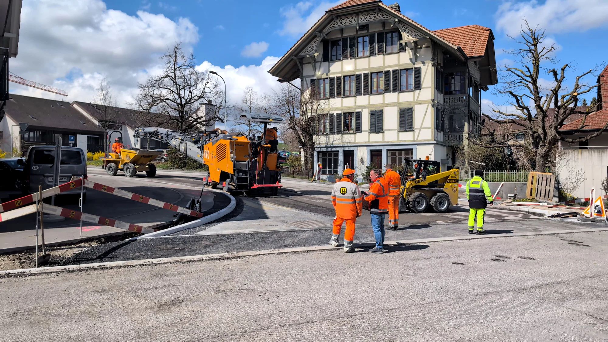 Junction with the surface milled off, construction machinery and workers in front of a historic building.