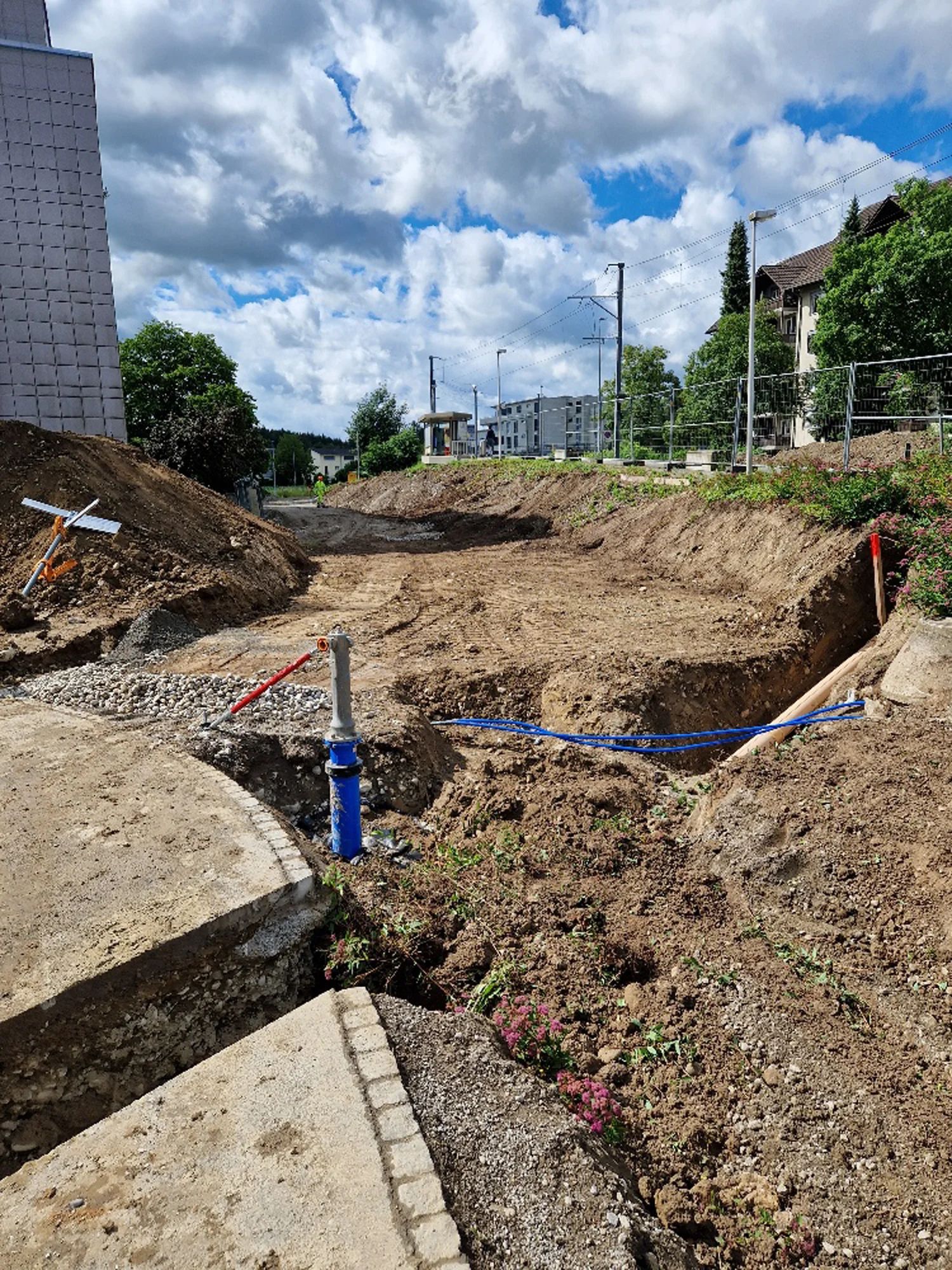 Excavated pit next to the stop with exposed utility lines, residential buildings behind.