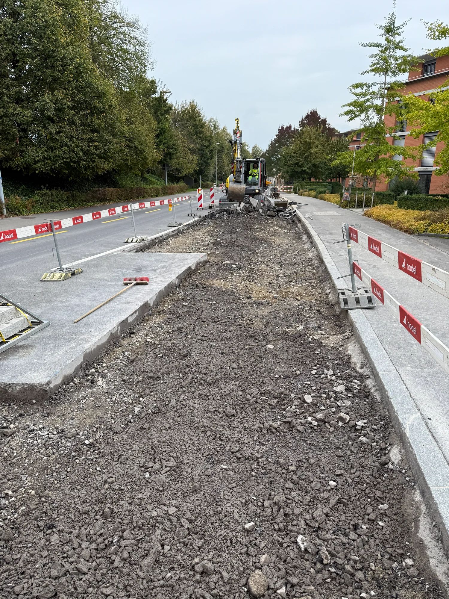 Broken-up road section with a new kerb, an excavator in the background.