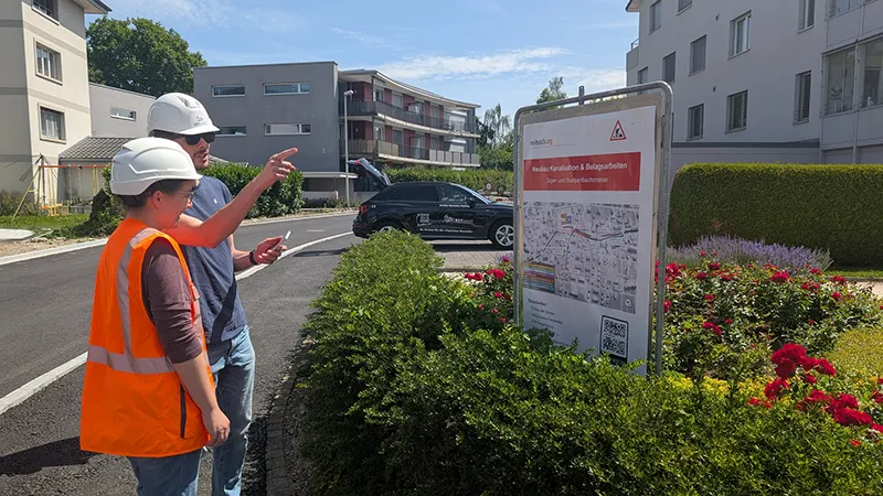 Two employees in front of a construction site sign, one pointing at it