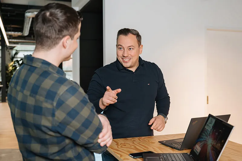 Two employees talking at a standing table with laptops