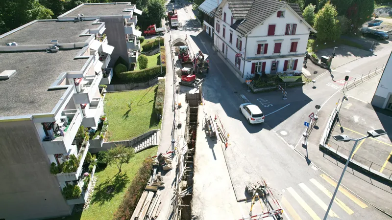 Aerial view of Sihlwaldstrasse: utility trench along the apartment buildings, excavators and site vehicles at the junction.